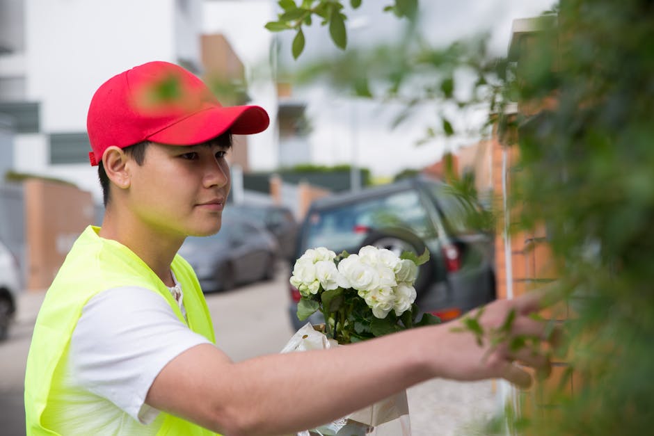A delivery person, wearing a bright yellow vest and a red cap, is seen closely inspecting and handing over a bouquet of fresh white flowers, likely roses, in a clear wrapping paper tied with a ribbon.